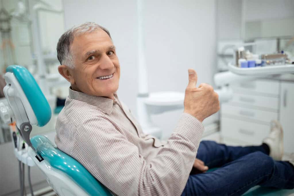 Ein Zahnarztpatient sitzt auf einem Behandlungsstuhl und zeigt den Daumen nach oben