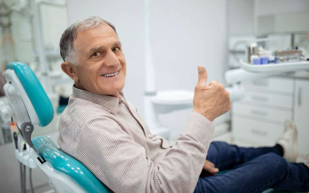 Ein Zahnarztpatient sitzt auf einem Behandlungsstuhl und zeigt den Daumen nach oben